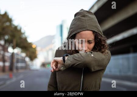 Kaukasische Frau hustet und trägt eine Smartwatch in den Straßen Stockfoto