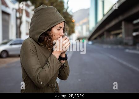 Kaukasische Frau hustet und trägt eine Smartwatch in den Straßen Stockfoto