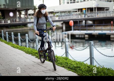 Kaukasische Frau mit einer Schutzmaske und einem Fahrradhelm in den Straßen, Radfahren in den Straßen Stockfoto