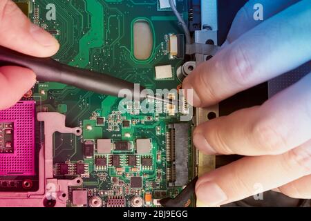 Mann repariert Computer. Ein Servicetechniker in Hemd repariert Laptop, am weißen Schreibtisch gegen weiße Wand. Computer-Motherboard Hintergrund mit Blur Neon Stockfoto