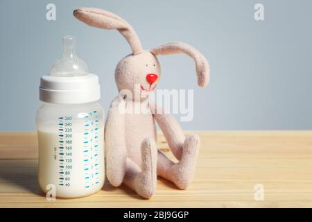 Babyflasche mit Milch mit Kaninchenspielzeug auf Holztisch Stockfoto