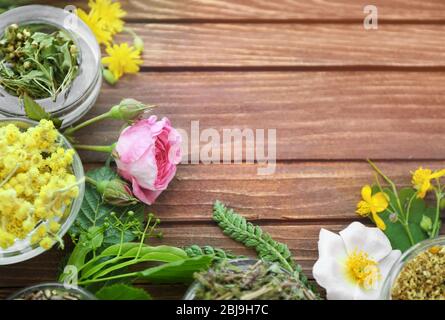 Kräuterauswahl und frische Blumen in Schalen auf Holzhintergrund Stockfoto