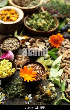 Kräuterauswahl und frische Blumen in Schalen auf Holzhintergrund Stockfoto