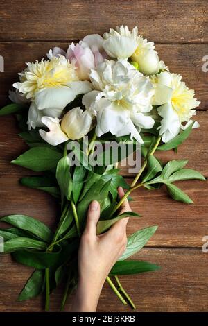 Weibliche Hand hält schöne weiße Pfingstrose Blumen auf Holzhintergrund Stockfoto