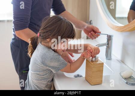 Kaukasischer Vater lehrt kleines Kind Mädchen, wie man Hände im Badezimmer während Covid-19 Pandemie Lockdown waschen. Papa und Baby Tochter waschen Hände bei si Stockfoto