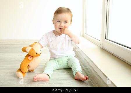 Baby sitzt mit Teddybär am Fenster im Zimmer Stockfoto