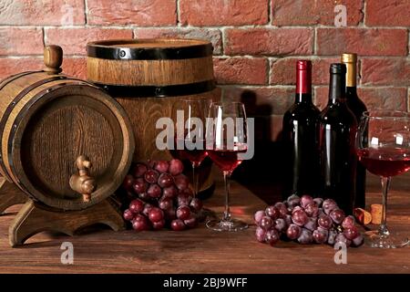 Gläser Rotwein, Trauben und Holzfässer auf Backstein-Wand Hintergrund Stockfoto