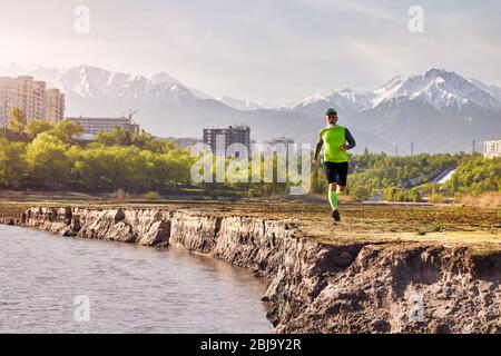 Ältere Mann in der Nähe des Flusses mit Gebäuden und Berg Hintergrund Am Morgen läuft. Gesunder Lebensstil Konzept Stockfoto