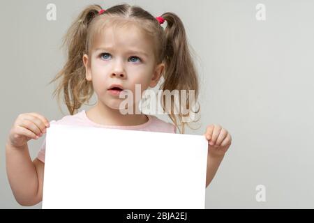 Fröhliches lächelndes Mädchen in rosa T-Shirt mit leerem Copyspace A4 Blatt Papier vor ihm, Komposition isoliert auf weißem Hintergrund Stockfoto