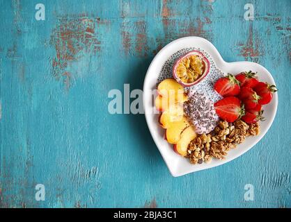 Gesundes Frühstück mit Früchten und Chia-Samen in herzförmiger Platte auf blauem Hintergrund Stockfoto