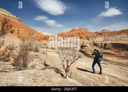 Tourist mit Rucksack und Kamera, die ein Bild aus der staubigen Canyons auf surreale roten Bergen gegen den blauen Himmel in der Wüste Stockfoto