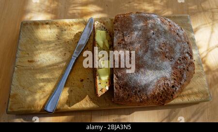 Hausgemachtes Brot sitzt auf dem Brottafel, eine Scheibe wurde zum Essen gebuttert Stockfoto