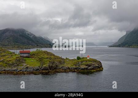 Eine norwegische Hütte und Leuchtturm auf einer kleinen Insel mitten in einem Fjord an einem nassen, bewölkten Tag mit geringer Wolke im Spätsommer. Stockfoto