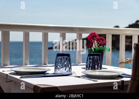 Tisch mit Stühlen und Tellern in einem Restaurant mit Blick auf das mittelmeer in sant Ulm, mallorca, spanien. Stockfoto