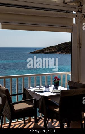 Tisch mit Stühlen und Tellern in einem Restaurant mit Blick auf das mittelmeer in sant Ulm, mallorca, spanien. Stockfoto