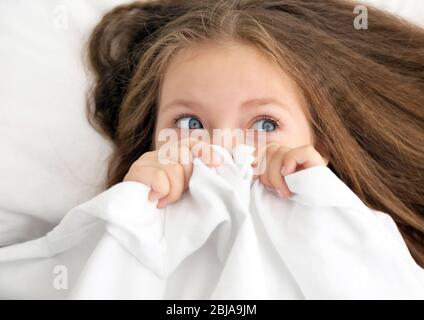 Nettes kleines Mädchen versteckt unter weißen Bettlaken Stockfoto