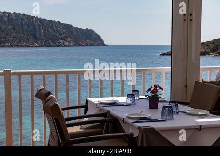 Tisch mit Stühlen und Tellern in einem Restaurant mit Blick auf das mittelmeer in sant Ulm, mallorca, spanien. Stockfoto