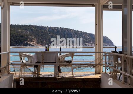Tisch mit Stühlen und Tellern in einem Restaurant mit Blick auf das mittelmeer in sant Ulm, mallorca, spanien. Stockfoto