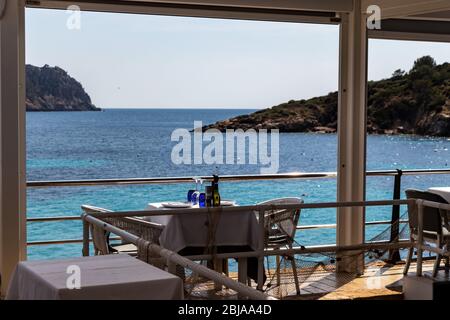 Tisch mit Stühlen und Tellern in einem Restaurant mit Blick auf das mittelmeer in sant Ulm, mallorca, spanien. Stockfoto