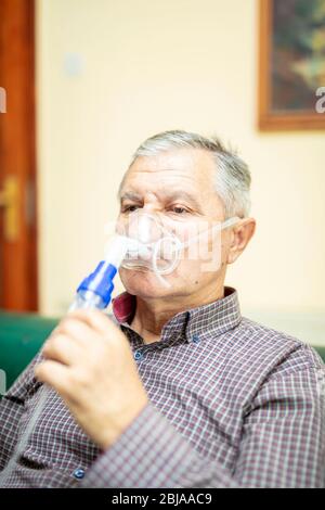 Leitender Mann, der medizinische Geräte für die Inhalation mit Atemschutzmaske verwendet, Vernebler im Zimmer Stockfoto