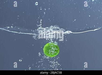 Frische saftige Limette fällt im Wasser auf dunklem Hintergrund Stockfoto