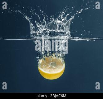 Die Hälfte der frischen Zitrone fällt auf dunklem Hintergrund in Wasser Stockfoto