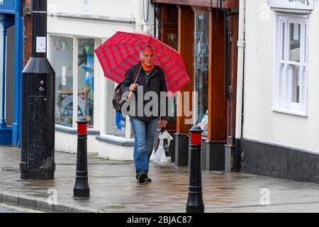 Bridport, Dorset, Großbritannien. April 2020. Wetter in Großbritannien. Ein Shopper mit Regenschirm, der sich an einem nassen Morgen in Bridport in Dorset vor dem Regen schützt. Bild: Graham Hunt/Alamy Live News Stockfoto