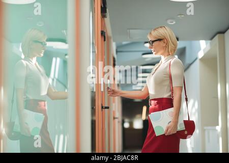Junge Geschäftsfrau in Brillen vor der Tür stehen und öffnen sie mit elektronischem Schlüssel im Büro Stockfoto