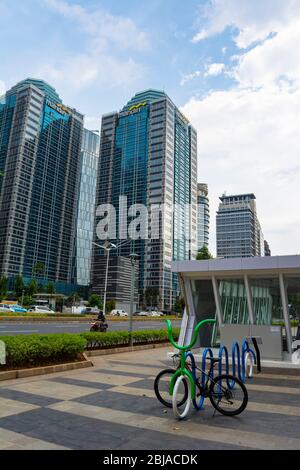 Gebäude in Sudirman Street, Central Business District in Jakarta. Im Vordergrund stehen ein Fahrrad und ein geschlossener MRT-Eingang. Stockfoto