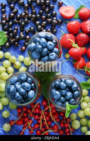 Gläser mit Früchten und Beeren auf Holztisch Stockfoto