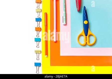 Blätter aus farbigem Papier, in einer Reihe angeordnet, Buntstifte, Scheren und Vorräte auf einem weißen Tisch. Kinderkunst, Handwerk für Kinder oder die Vorbereitung eines Kindes für sc Stockfoto