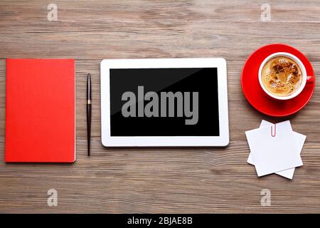 Tablette mit Tasse Kaffee und Bürogeräte auf Holzhintergrund Stockfoto