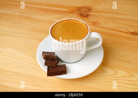 Nahaufnahme eine Tasse Espresso Kaffee mit dunklen Schokoladenwürfeln isoliert auf Holztisch Stockfoto