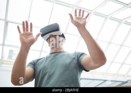 Mann trägt virtuelle Brille in Videospielen er stehend und gestikuliert Stockfoto