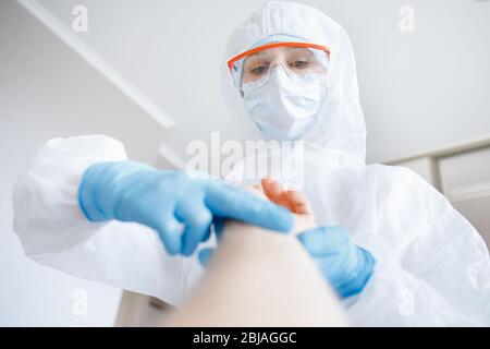 Arzt in Biohazard überprüft Puls des Patienten in Quarantäne Symptome von Coronavirus im Bett Stockfoto