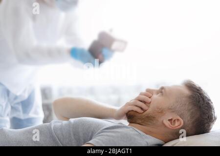 Temperaturmessung bei Coronavirus-Patienten. Arzt misst Mann mit Thermometer und macht Behandlung Stockfoto