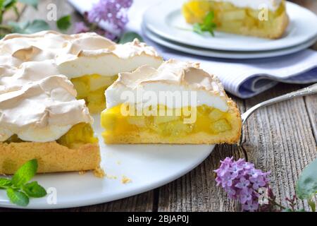 Köstliche Rhabarber-Kuchen mit süßem Baiser auf einem Holztisch mit frühlingshafter lila Dekoration serviert Stockfoto