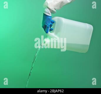 Hand in Handschuh gießen Wasser aus Kanister auf grünem Hintergrund Stockfoto