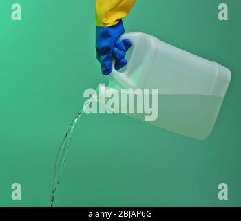 Hand in Handschuh gießen Wasser aus Kanister auf grünem Hintergrund Stockfoto