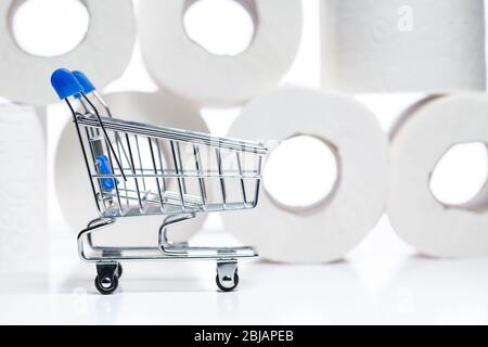 Lebensmitteleinkaufwagen mit Toilettenpapierrollen dahinter. Konzept des Mangels an Toilettenpapier in den Geschäften aufgrund Coronavirus, Covid-19 Stockfoto