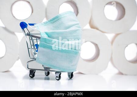 Schutzmaske und Lebensmitteleinkaufskart mit Toilettenpapier Rollen hinter. Konzept des Mangels an Toilettenpapier in den Geschäften wegen Coronavirus, Covid- Stockfoto