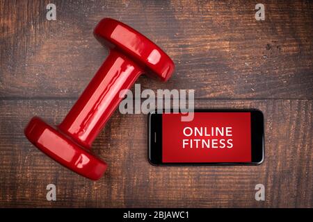 Rote Hantel und Smartphone auf einem Holzhintergrund. App für das Training in Innenräumen. Online-Fitnessprogramm. Home Online-Workout. Draufsicht, Covid-19 Coronavi Stockfoto
