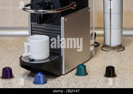 Espresso auf einer automatischen Maschine mit Aluminiumkapseln zubereiten. Bunte Metallschoten um die Kaffeemaschine und eine weiße Tasse, um heißen, tropfenden Kaffee zuzubereiten. Stockfoto