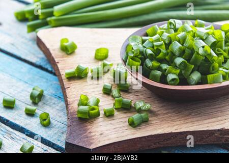 Frische grüne Zwiebel gehackt und liegt auf einer Schüssel auf einem Schneidebrett auf einem Hintergrund von blauen Brettern. Zwiebeln sind reich an Vitaminen und Mineralstoffen. Stockfoto