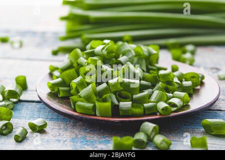 Frische grüne Zwiebel gehackt und liegt auf einer Schüssel auf einem Hintergrund von blauen Brettern. Schnittlauch hat viele Vitamine und Mineralstoffe. Stockfoto