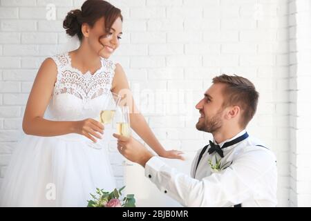Bräutigam und Braut mit Gläsern Champagner auf weißem Backstein-Wandhintergrund Stockfoto