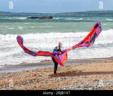 Garrettstown, Cork, Irland. April 2020. Ein Einheimischer kämpft, um seinen Drachen bei hohem Wind zu kontrollieren, während er sich auf einen Morgen des Surfens am Garrettstown Beach in Co. Cork, Irland, vorbereitet. - Credit; David Creedon / Alamy Live News Stockfoto