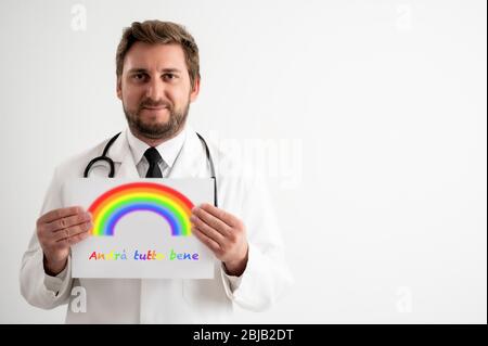 Porträt des männlichen Arztes mit Stethoskop in medizinischer Uniform, das ein weißes Papier mit Regenbogenbotschaft hält und lächelnd auf einem weißen isolierten Rückgro posiert Stockfoto