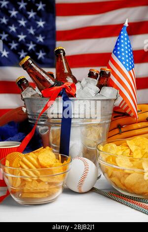 Eimer mit Bierflaschen, Chips und Kugel auf weißem Holztisch Stockfoto