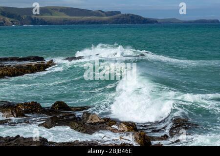 Wellen, die an einem stürmischen Tag in Waikawa, Neuseeland, bei Rocks in Porpoise Bay of New Zealand zerquetschen. Stockfoto